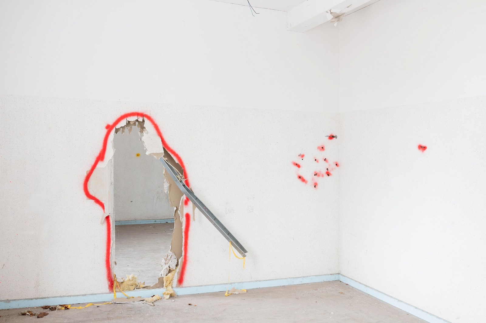 Lager Heuberg, Stetten am kalten Markt. Wanddurchbruch und Einschusslöcher. Die mit roter Sprühfarbe aufgetragene Markierung verdeutlicht den Instandsetzungsbedarf, um den Raum in seinen ursprünglichen Zustand zurückzuversetzen.